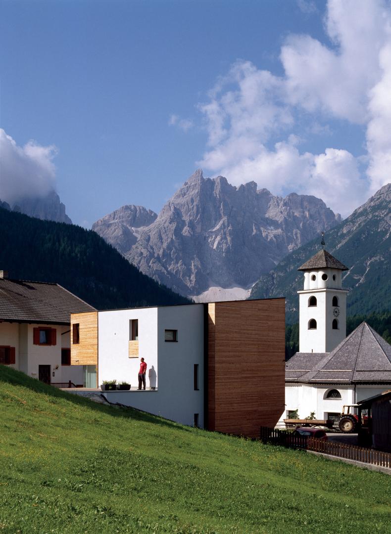 Residencia blanca y de madera con iglesia y montañas al fondo