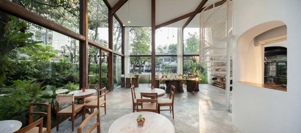 Showroom en verre avec structure en bois. La transparence révèle un luxuriant jardin environnant