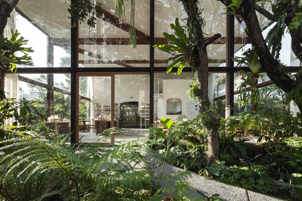 Showroom en verre avec structure en bois. La transparence révèle un luxuriant jardin environnant