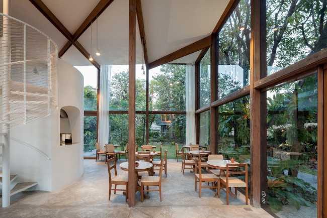 Showroom en verre avec structure en bois. La transparence révèle un luxuriant jardin environnant