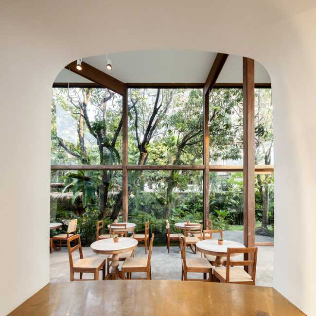 Showroom en verre avec structure en bois. La transparence révèle un luxuriant jardin environnant