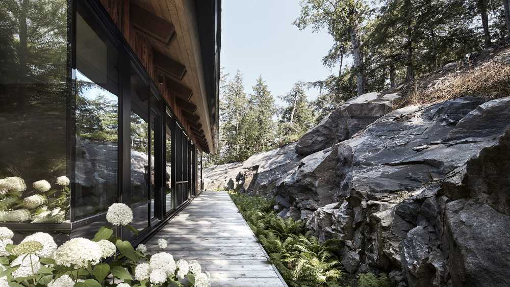 Un'enclave rocciosa accoglie un cottage in legno. Rimessa per barche sulle rive di un lago