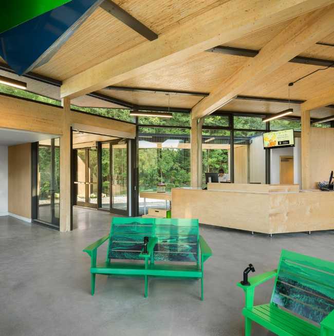 Interior de madera con asientos verdes y paredes de vidrio que dan al paisaje