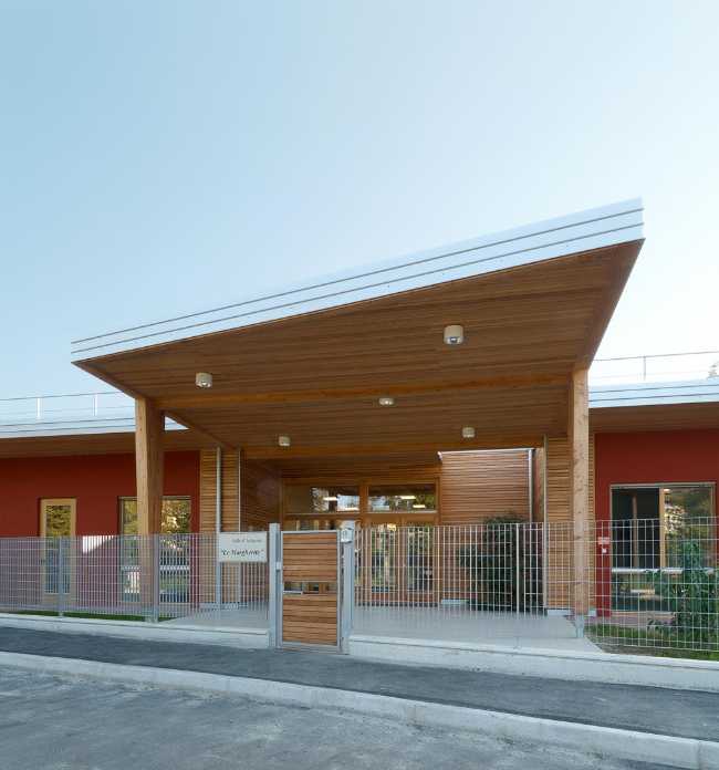 Ingresso di un asilo nido con una tettoia in legno illuminata