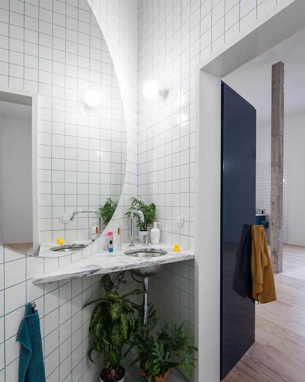 Bagno triangolare con piastre bianche porta blu e specchio rotondo